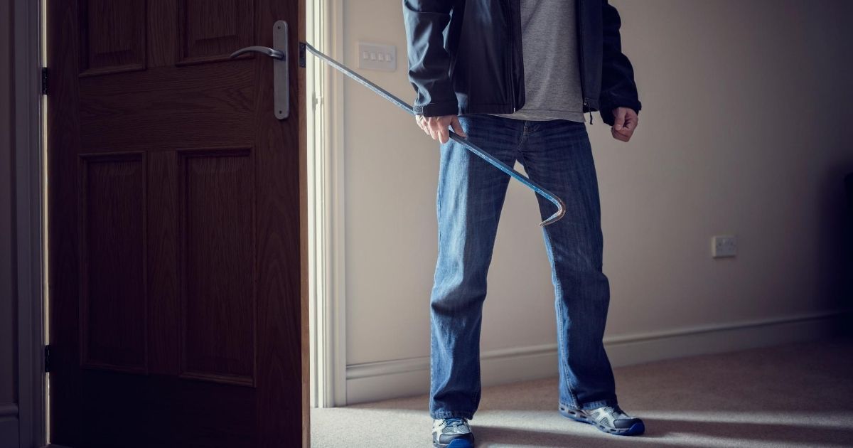 Πόρτα χωρίς κλειδαριά ασφαλείας παραβιασμένη από άντρα που κρατάει σιδερένιο λοστό.