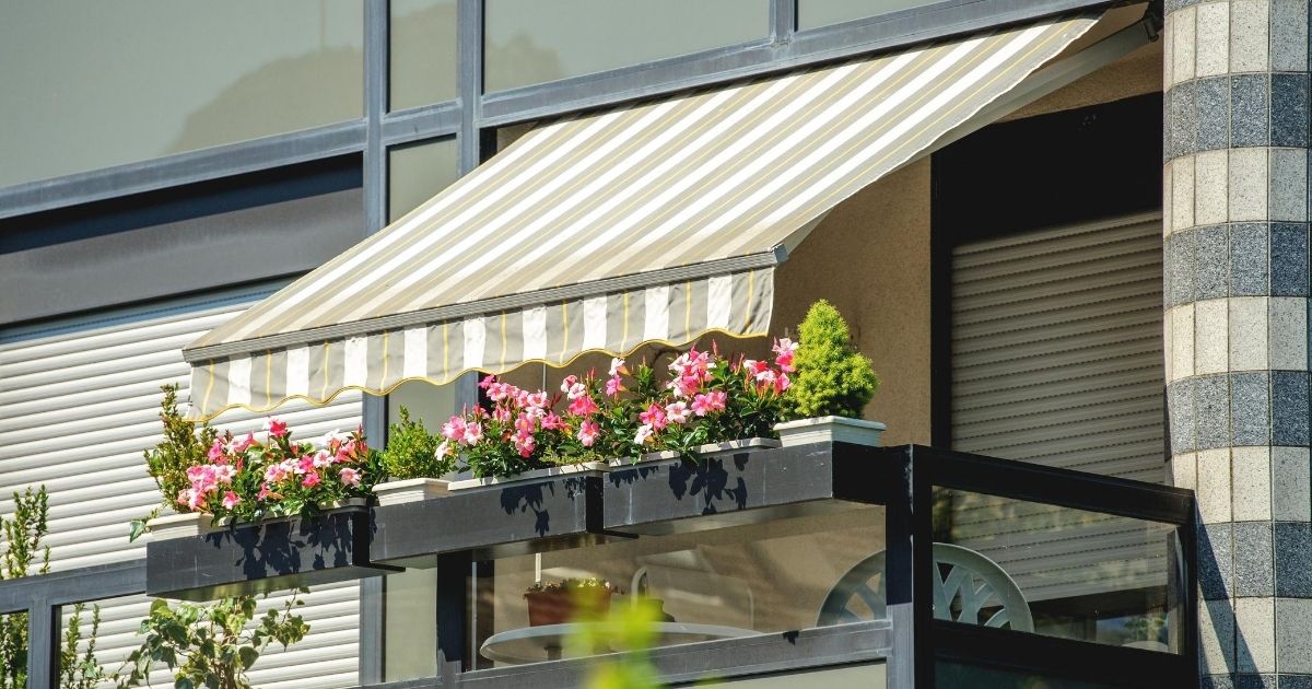Βλέπουμε ένα μπαλκόνι με λουλούδια και τέντα