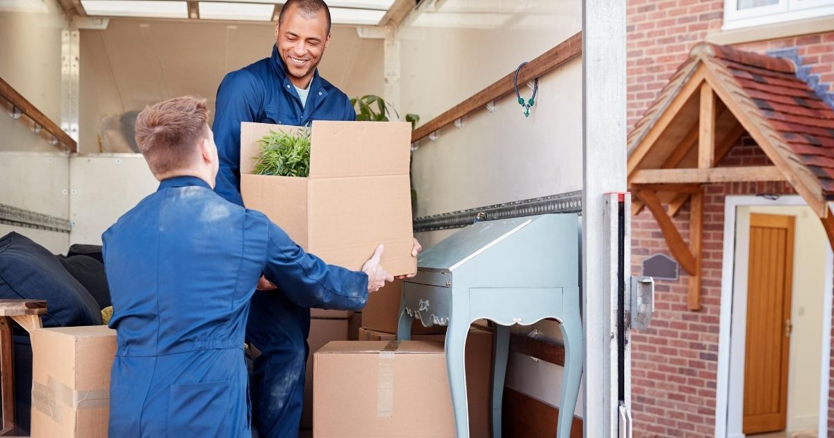 Δύο επαγγελματίες μεταφέρουν χάρτινες κούτες μέσα σε σπίτι. 