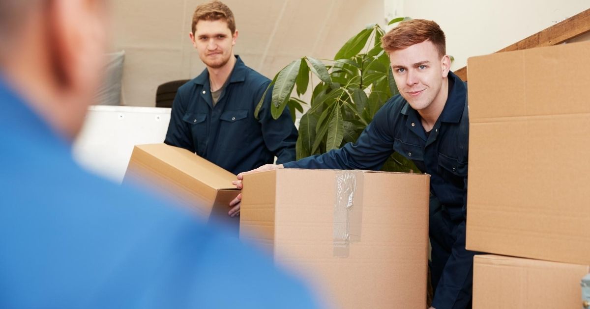 Επαγγελματίες μέσα σε σπίτι μεταφέρουν χάρτινες κούτες.