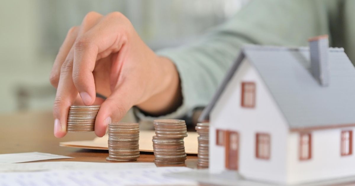 Πάνω σε τραπέζι τεσσερις στίβες κερμάτων, δίπλα σε μακέτα σπιτιού.