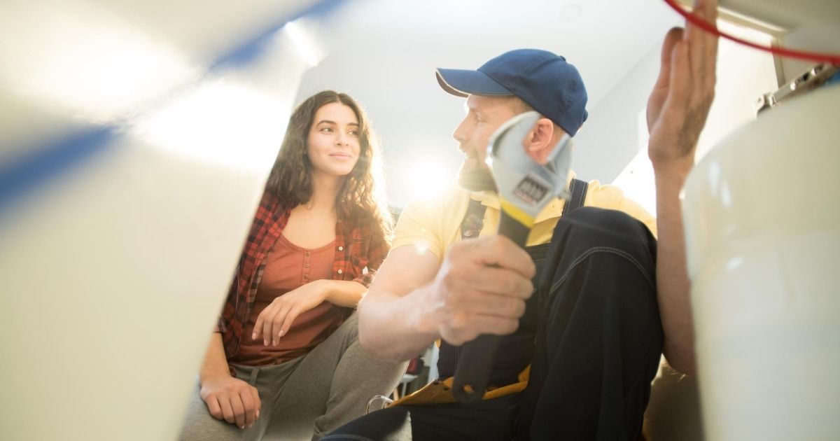 Ένας επαγγελματίας γονατιστός και κρατώντας μια τανάλια, δείχνει σε μια γυναίκα.