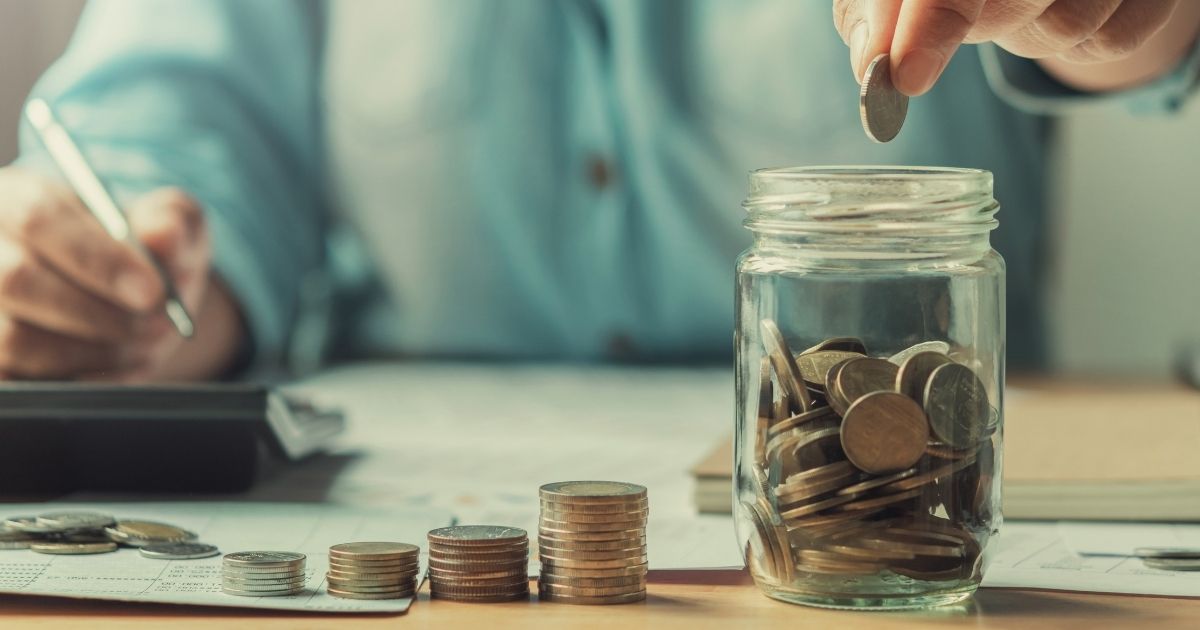 Ένα γυάλινο βάζο με ένα χέρι που ρίχνει μέσα κέρματα και κέρματα δίπλα στο βάζο