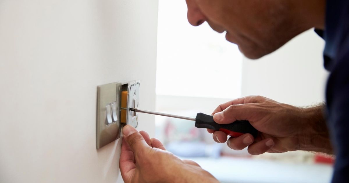 Ένας άντρας κρατώντας κατσαβίδι ελέγχει διακόπτη φώτων σε τοίχο.