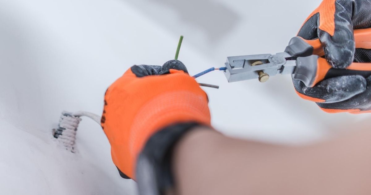 Ένας επαγγελματίας φορώντας γάντια, επισκευάζει με πένσα, καλώδια παροχής γραμμής τηλεφώνου σε τοίχο.