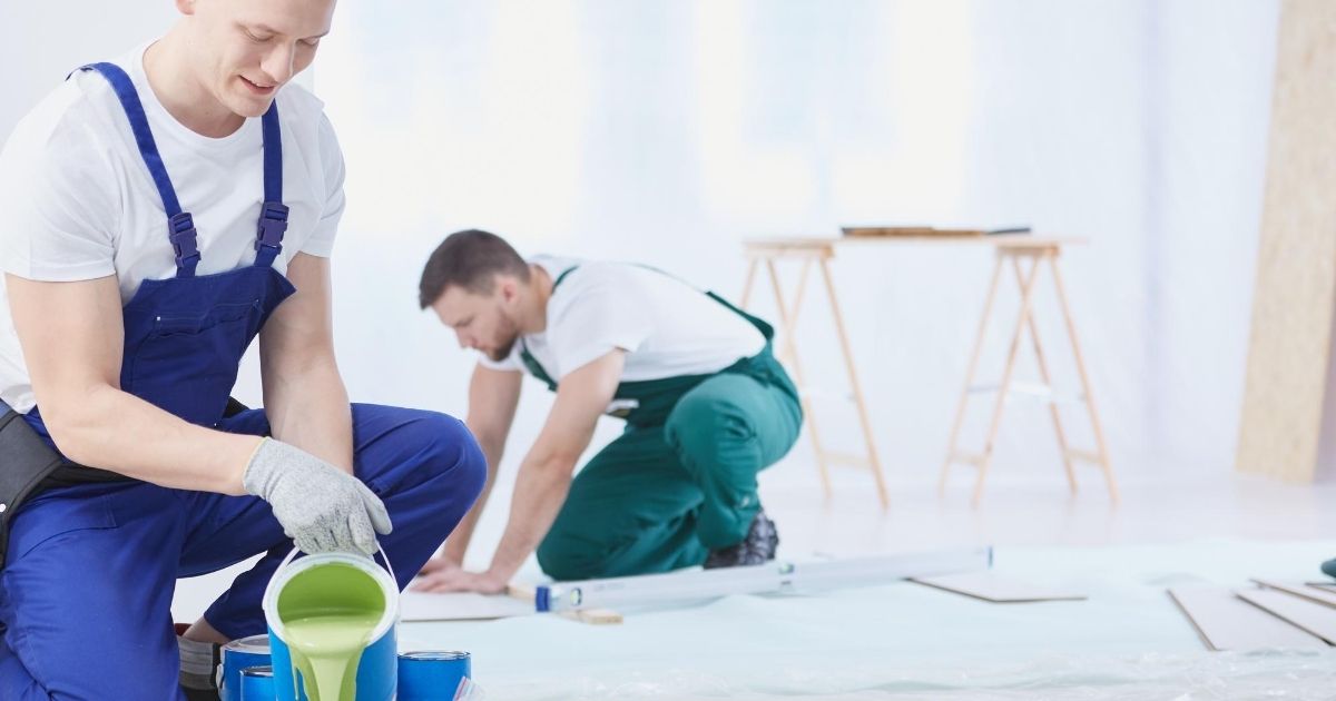 Δύο ανδρες τεχνικοί εργάζονται γονατισμένο σε πάτωμα. Δίπλα σκάλα και διάφορα εργαλεία.