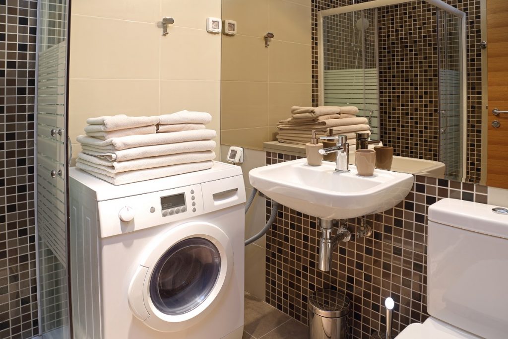 Εσωτερικό μπάνιου σπιτιού με πλυντήριο. Επάνω στο πλυντήριο και στον νιπτήρα έχει πολλές διπλωμένες πετσέτες.