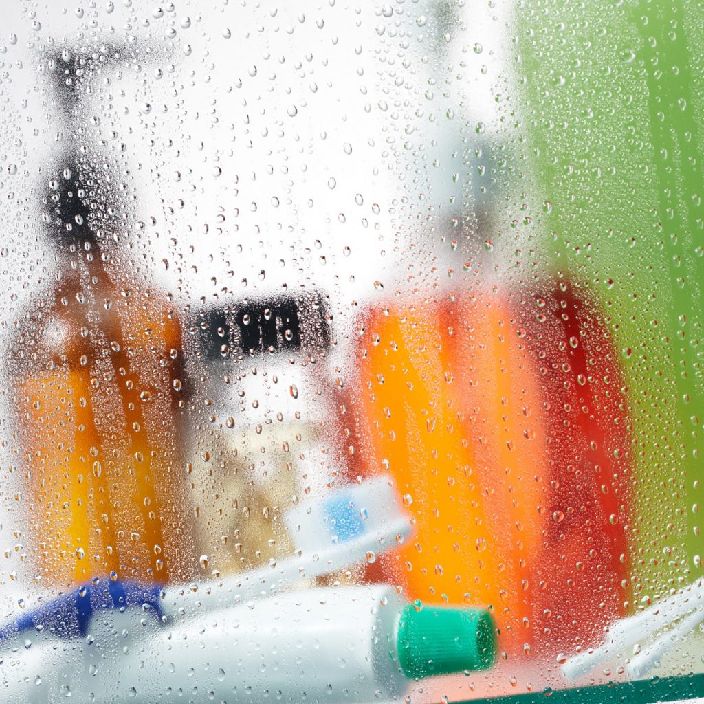 Ένα τζάμι μπάνιου θολό από στάλες νερού και υγρασία. Διακρίνονται μπουκάλια και οδοντόκρεμα με οδοντόβουρτσα.