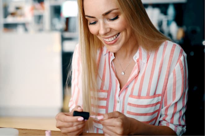 Μια γυναίκα βάφει τα νύχια του χεριού της με ροζ μανό χαμογελώντας.