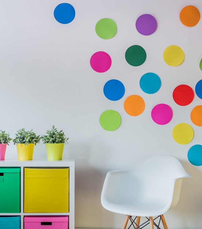Δωμάτιο με πολύχρωμο έπιπλο που έχει επάνω γλάστρες σε διάφορα χρώματα. Ο τοίχος λευκός με κύκλους σε διάφορα χρώματα.
