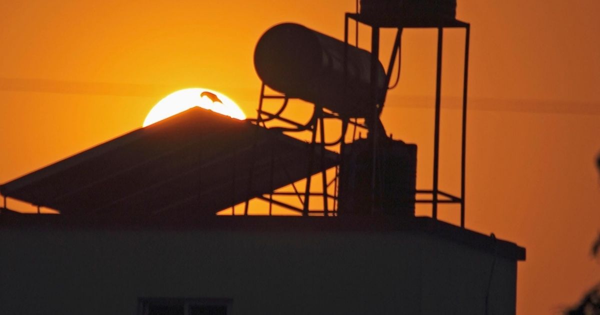 Ένας ηλιακός θερμοσίφωνας τοποθετημένος σε ταράτσα. Πίσω του ο ήλιος ανατέλει.